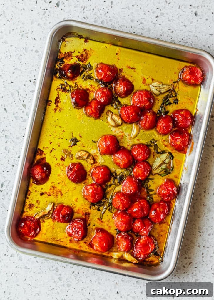 A silver sheet pan of roasted cherry tomatoes on a white counter.