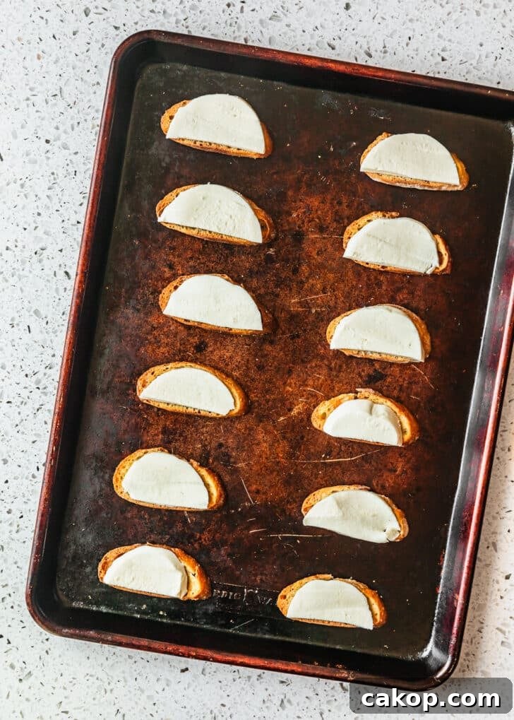 A sheet pan of crostini with mozzarella on a white counter.
