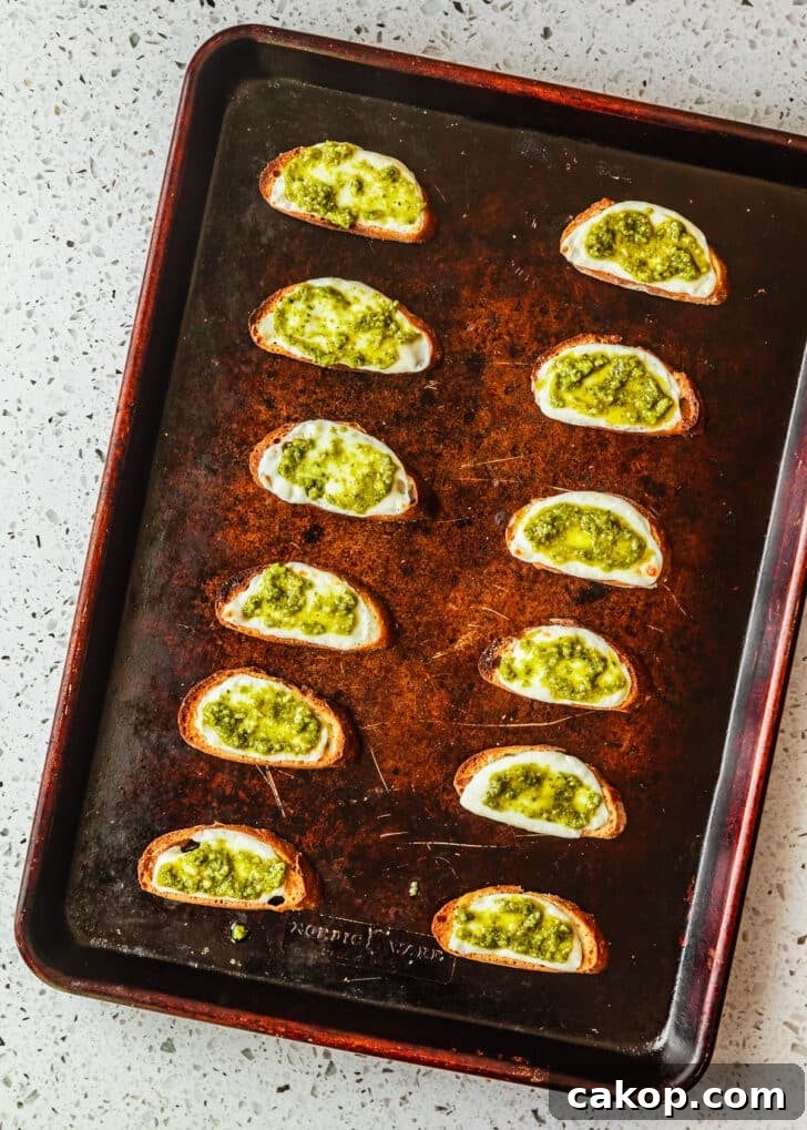 A sheet pan of crostini with mozzarella and pesto on a white terrazzo counter.