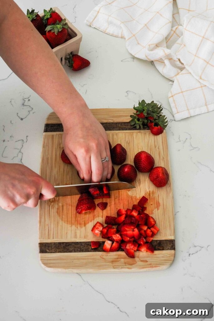 Homemade Strawberry Ice Cream Recipe with Fresh Berries 4 A woman dices strawberries on a wooden cutting board.