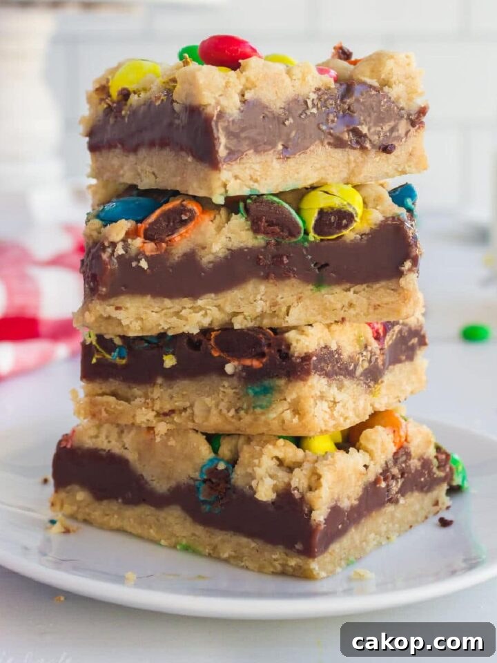 Close up of a stack of M&M Chocolate oat bars with a glass of milk in the background.