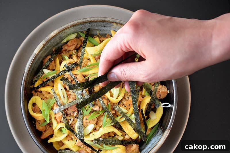 Kimchi Cauliflower Fried Rice — Whole30 & Gluten-Free Recipe 9 Someone adding slices of seaweed in a bowl with paleo kimchi cauliflower fried rice.