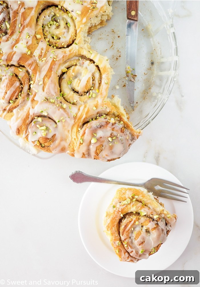Pistachio Cinnamon Rolls Drizzled with Tahini Glaze 3 Freshly baked rolls in baking dish and one on small dish.