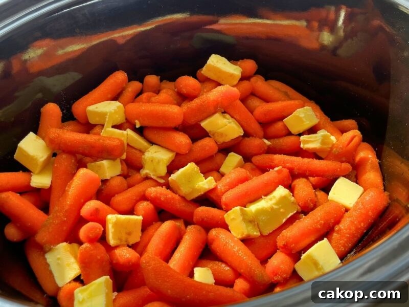A close-up view of baby carrots with cubes of butter in a cooking pot.