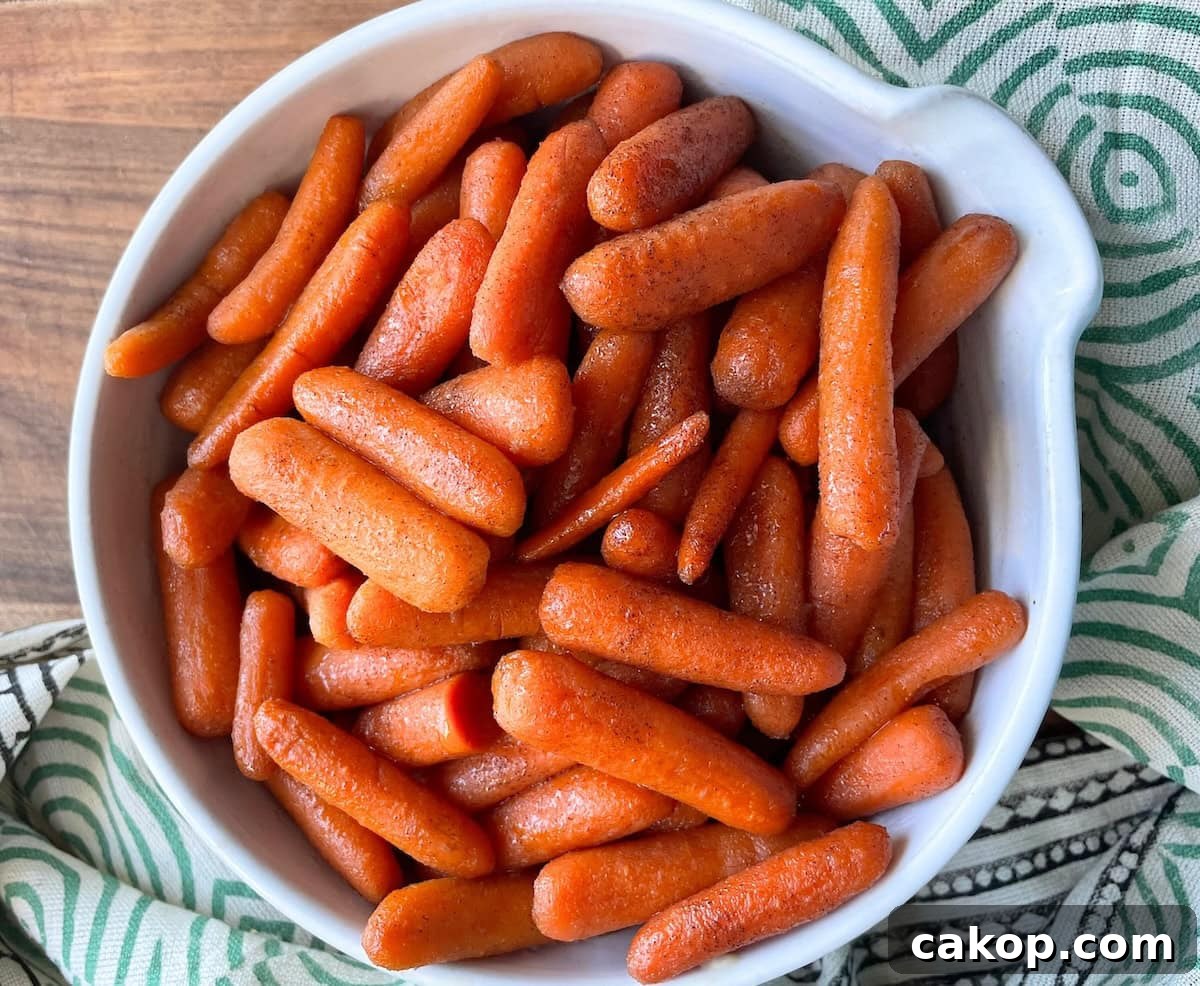 A white bowl filled with orange glazed baby carrots on a green-striped cloth.