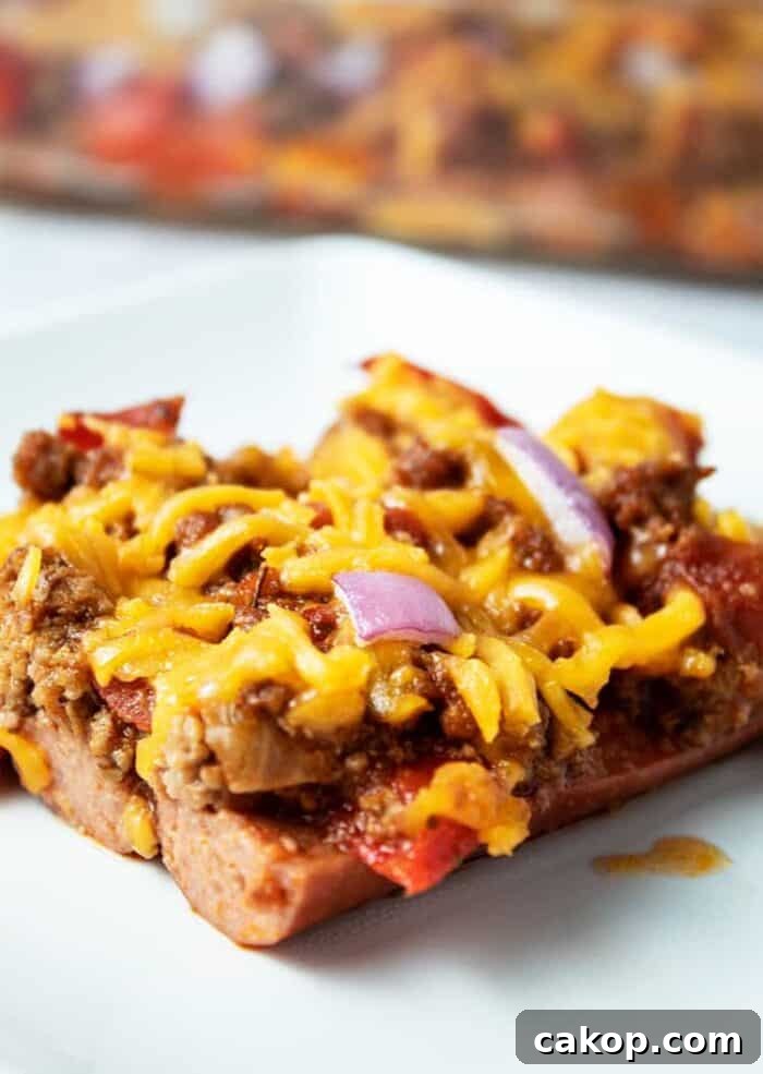 piece of keto chili dog casserole on a white plate with casserole dish in background