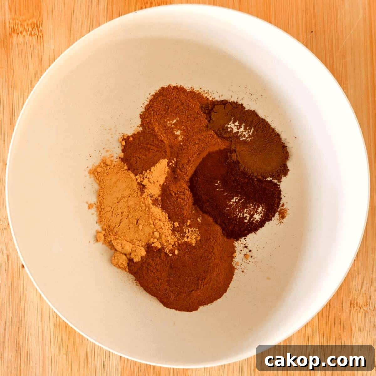 The ingredients to make pumpkin pie spice in a white bowl.