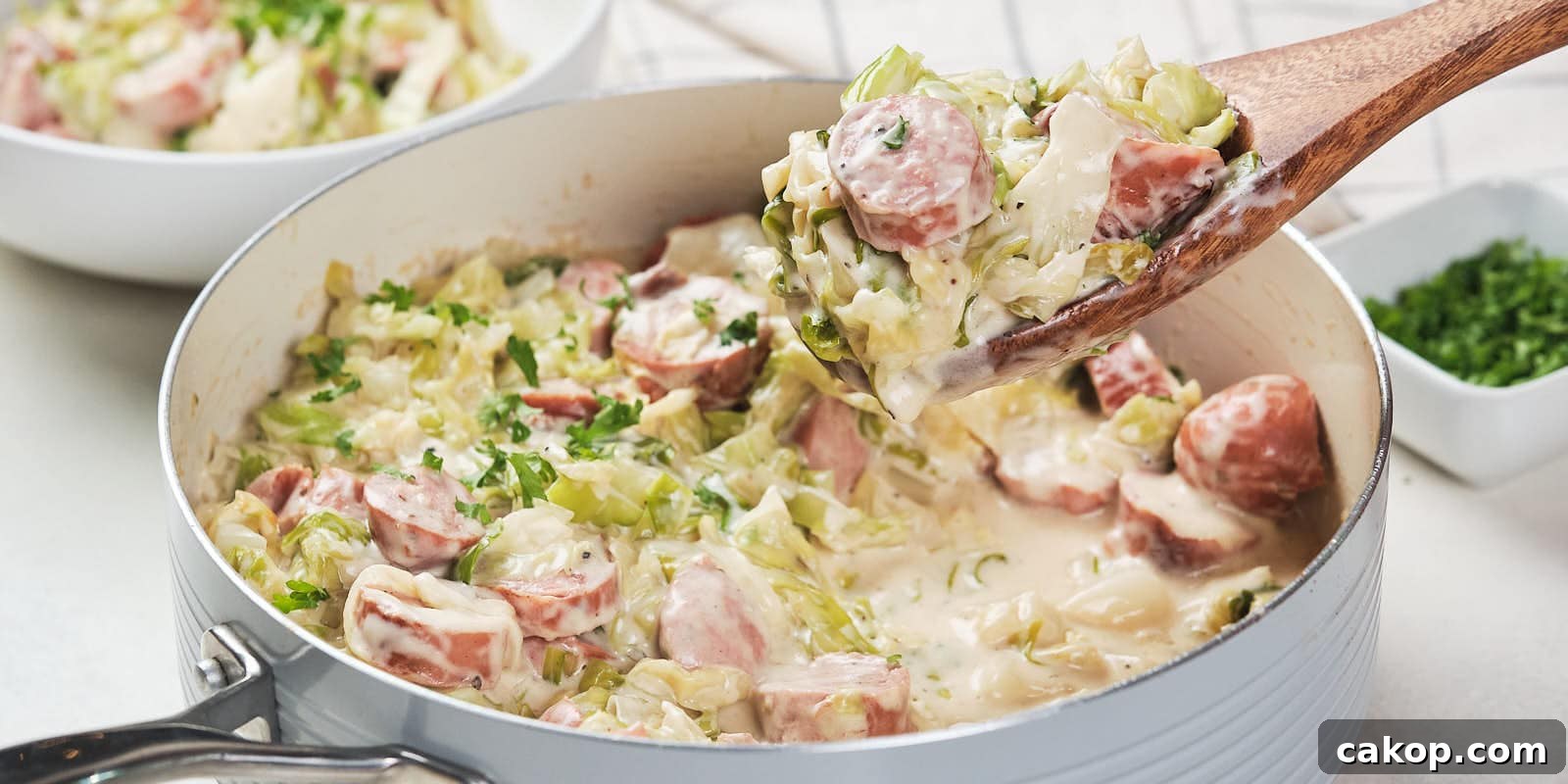 A skillet containing a creamy cabbage and sausage alfredo garnished with herbs.
