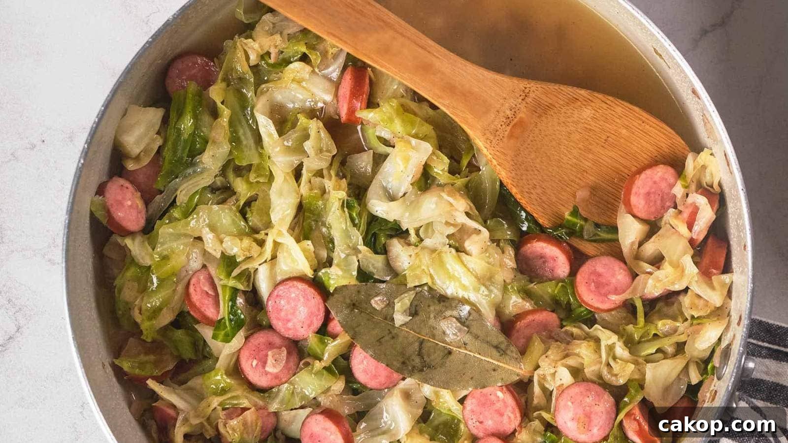 A pan filled with fried cabbage and sausage, with a wooden spoon resting inside.