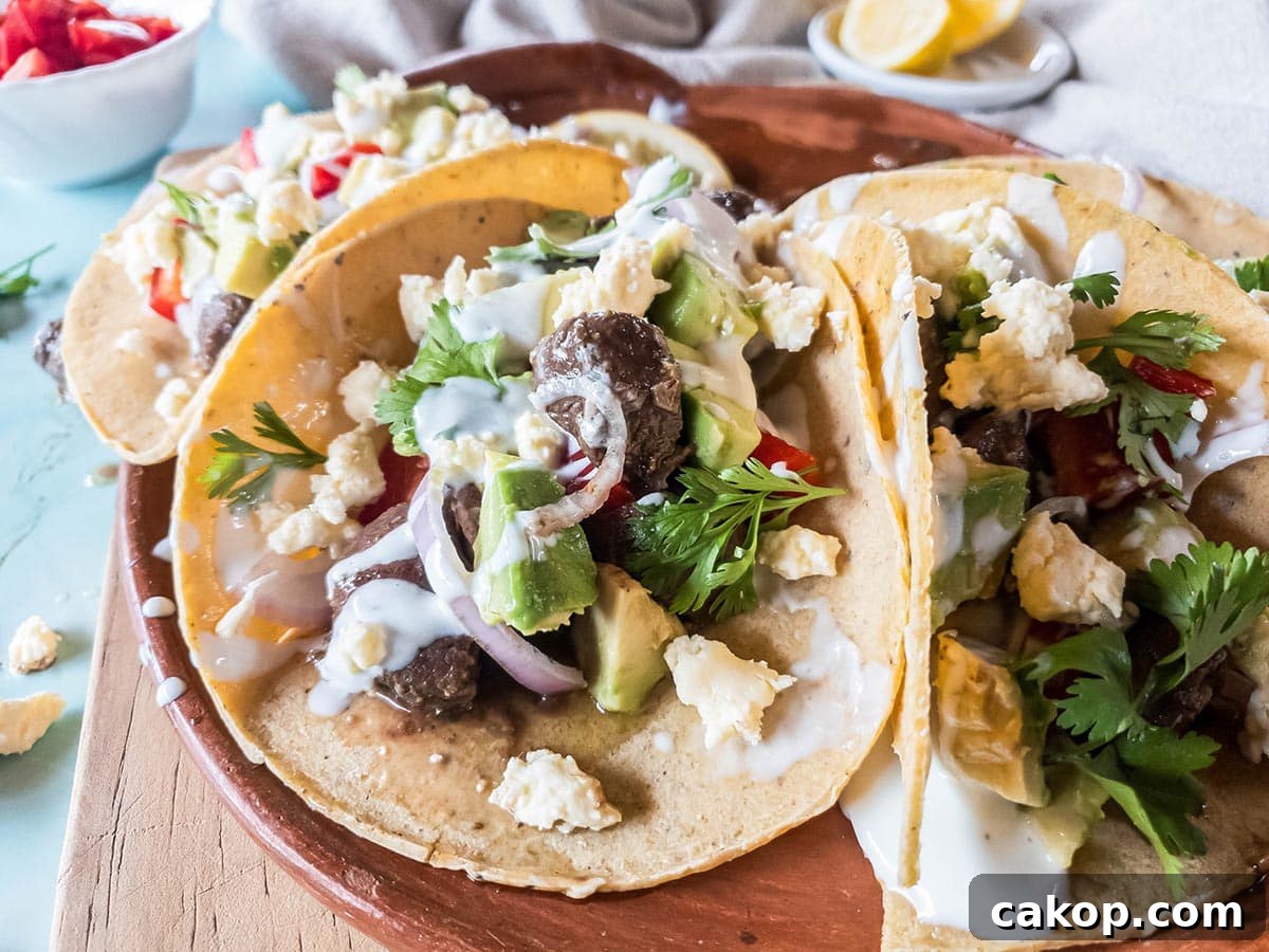 A picture of beef heart tacos with sour cream, avocado, red onion, and cilantro.