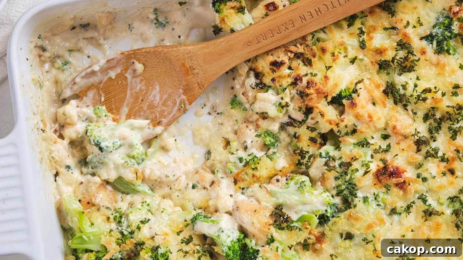A wooden spoon scooping chicken broccoli alfredo casserole out of a serving dish.