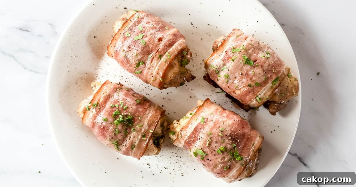 Four bacon-wrapped chicken thighs with parsley garnish on white plate.