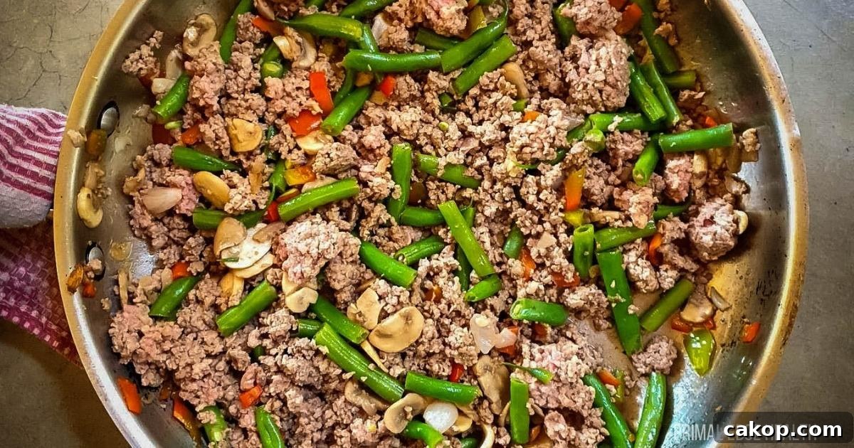 A picture of ground beef and green bean stir-fry in stainless steel skillet.
