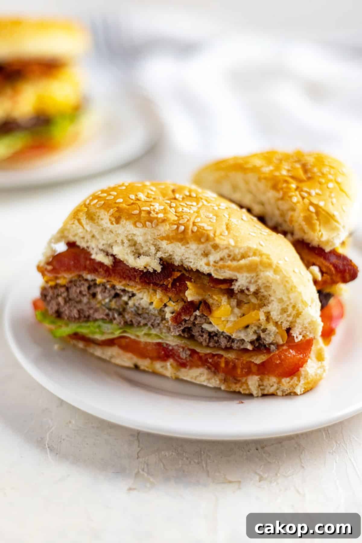 Stuffed Cheeseburgers Recipe: Juicy Bacon-Cheddar Burgers 2 cut in half cheesy stuffed burger topped with bacon and pimento cheese and lettuce and tomato on white plate