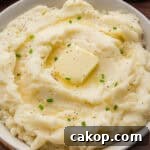 Classic Old-Fashioned Mashed Potatoes Recipe for Creamy Comfort 11 Creamy old-fashioned mashed potatoes in a bowl, topped with a square of butter, melted butter, black pepper, and chopped chives.