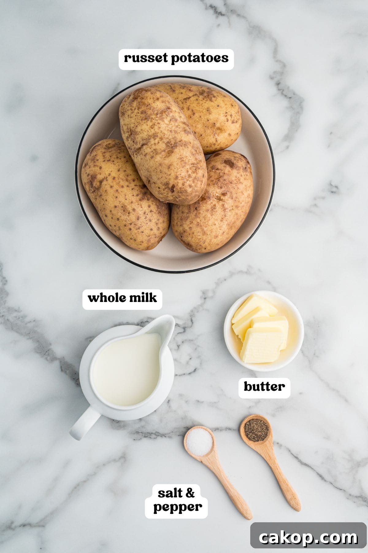 Classic Old-Fashioned Mashed Potatoes Recipe for Creamy Comfort 4 Labeled ingredients: a bowl of russet potatoes, a small pitcher of whole milk, a dish of butter slices, and two wooden spoons with salt and pepper.