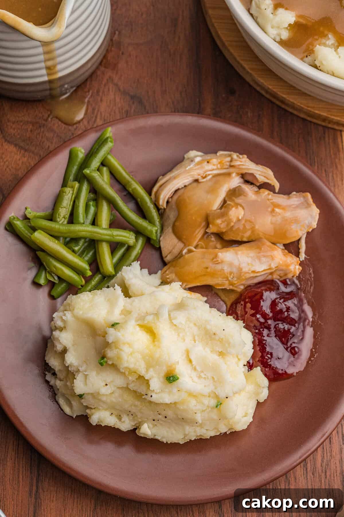 Classic Old-Fashioned Mashed Potatoes Recipe for Creamy Comfort 8 Dinner plate containing mashed potatoes with chives and melted butter, cooked green beans, turkey slices with brown gravy, and cranberry sauce.