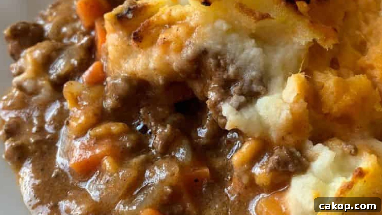 A plate with cottage pie casserole and a side of mixed greens on a white surface, accompanied by an orange-patterned cloth in the background.
