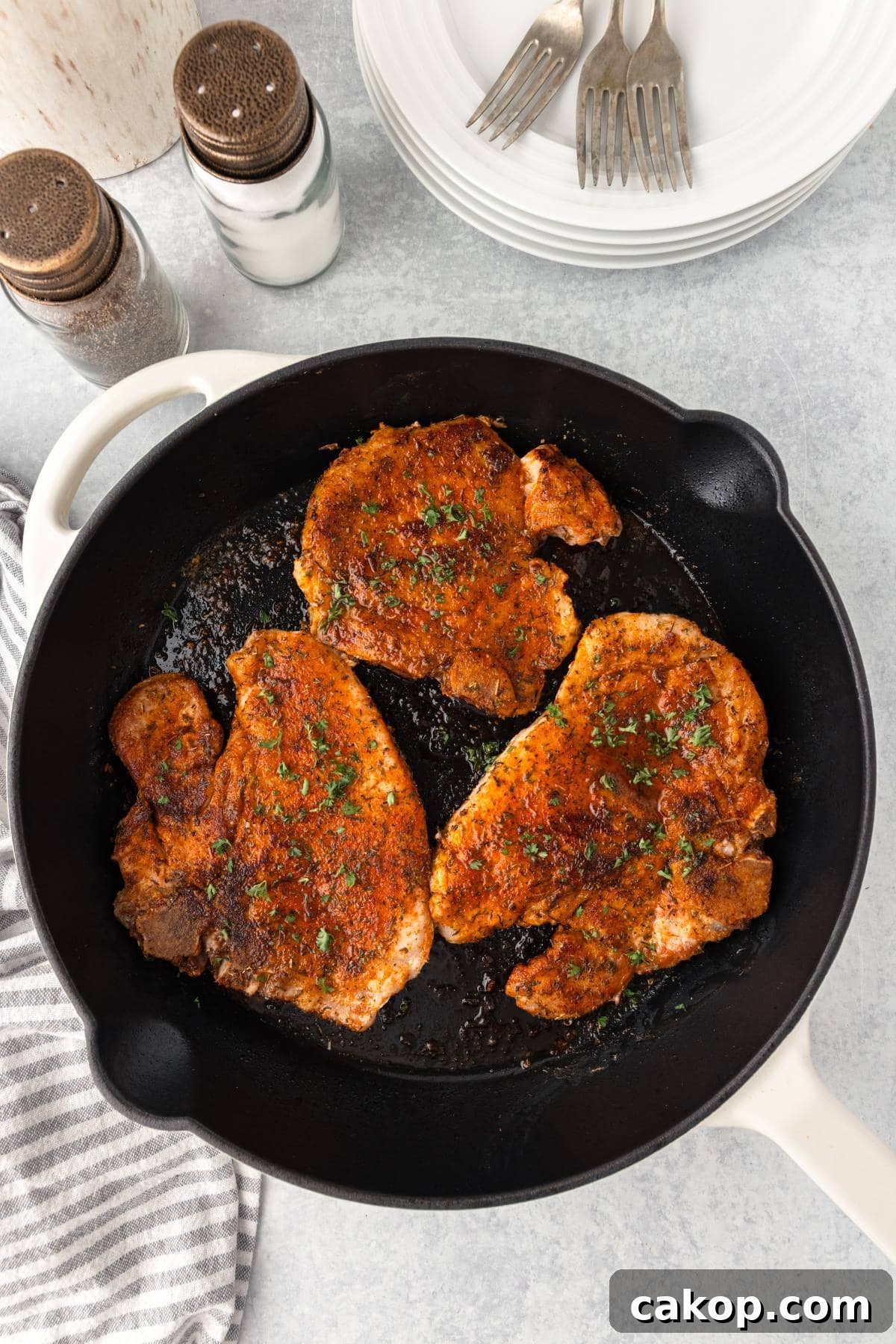 Juicy Bone-In Pork Chops: Simple Step-by-Step Cooking Guide 5 Juicy, seasoned pork chops cooking in a black skillet, garnished with fresh herbs.
