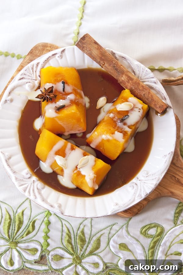 Candied Mexican Pumpkin (Calabaza en Tacha) Recipe 2 Calabaza en Tacha a.k.a. Candied Pumpkin with pilloncillo syrup and drizzled with sweetened condensed milk on a white plate atop a wooden cutting board on a sage green and white embroidered tea towel