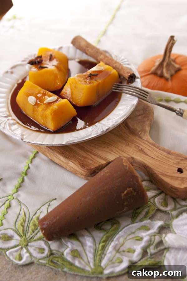 Candied Mexican Pumpkin (Calabaza en Tacha) Recipe 3 45 degree angle shot of mexican candied pumpkin wedges on a white plate with a puddle of brown syrup and drizzled with sweetened condensed milk on a white plate on a wooden cutting board with a pumpkin and a cinnamon stick