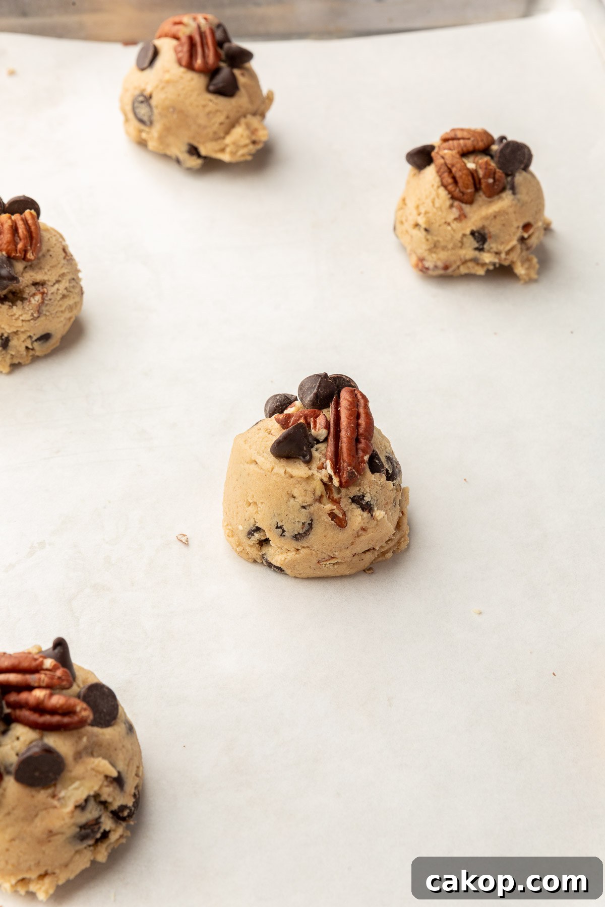 A close up of gluten-free pecan chocolate chip cookie dough balls on a baking sheet lined with parchment paper before baking in the oven.