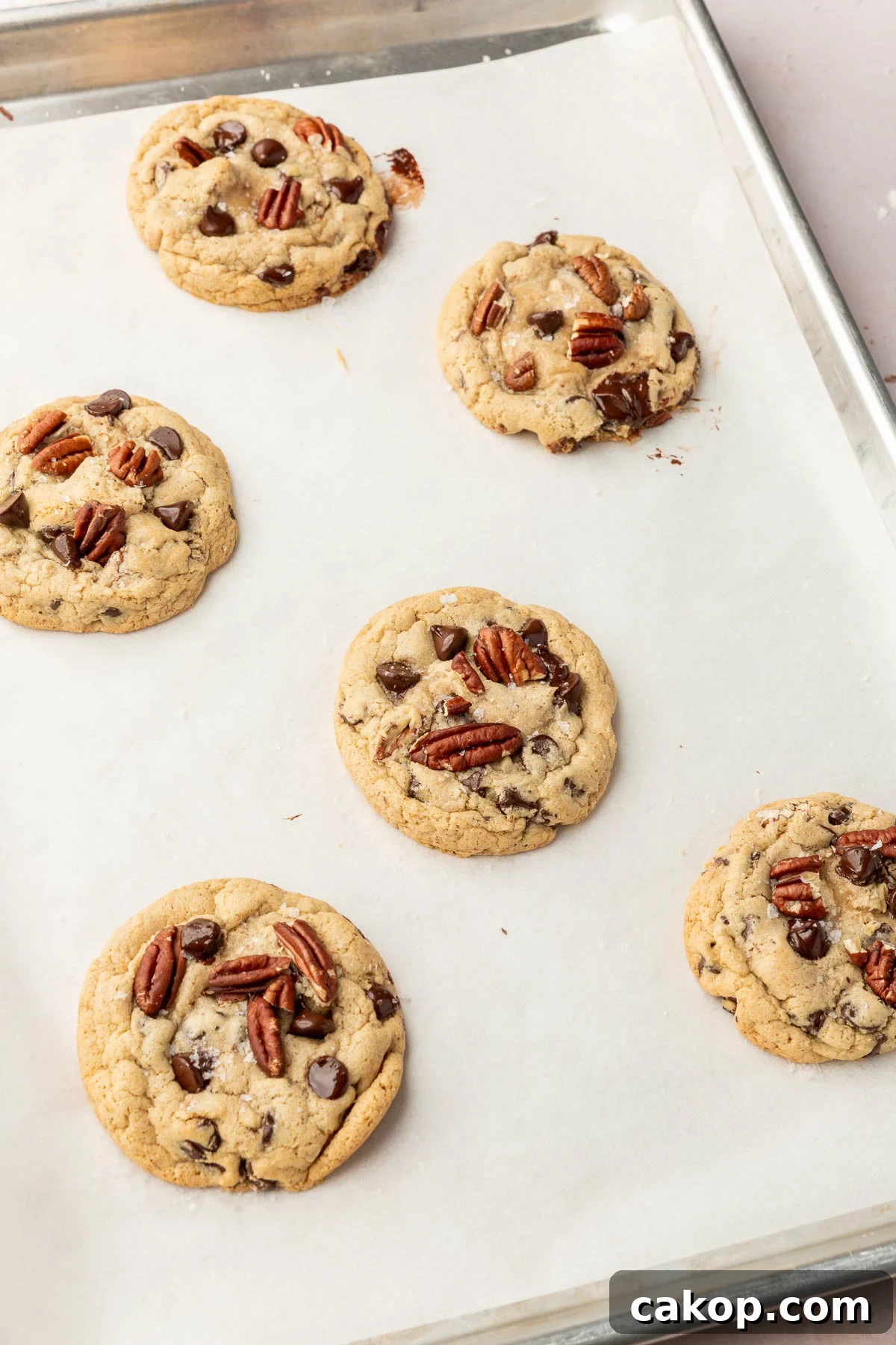 Six gluten-free pecan chocolate chip cookies on a baking sheet lined with parchment paper.