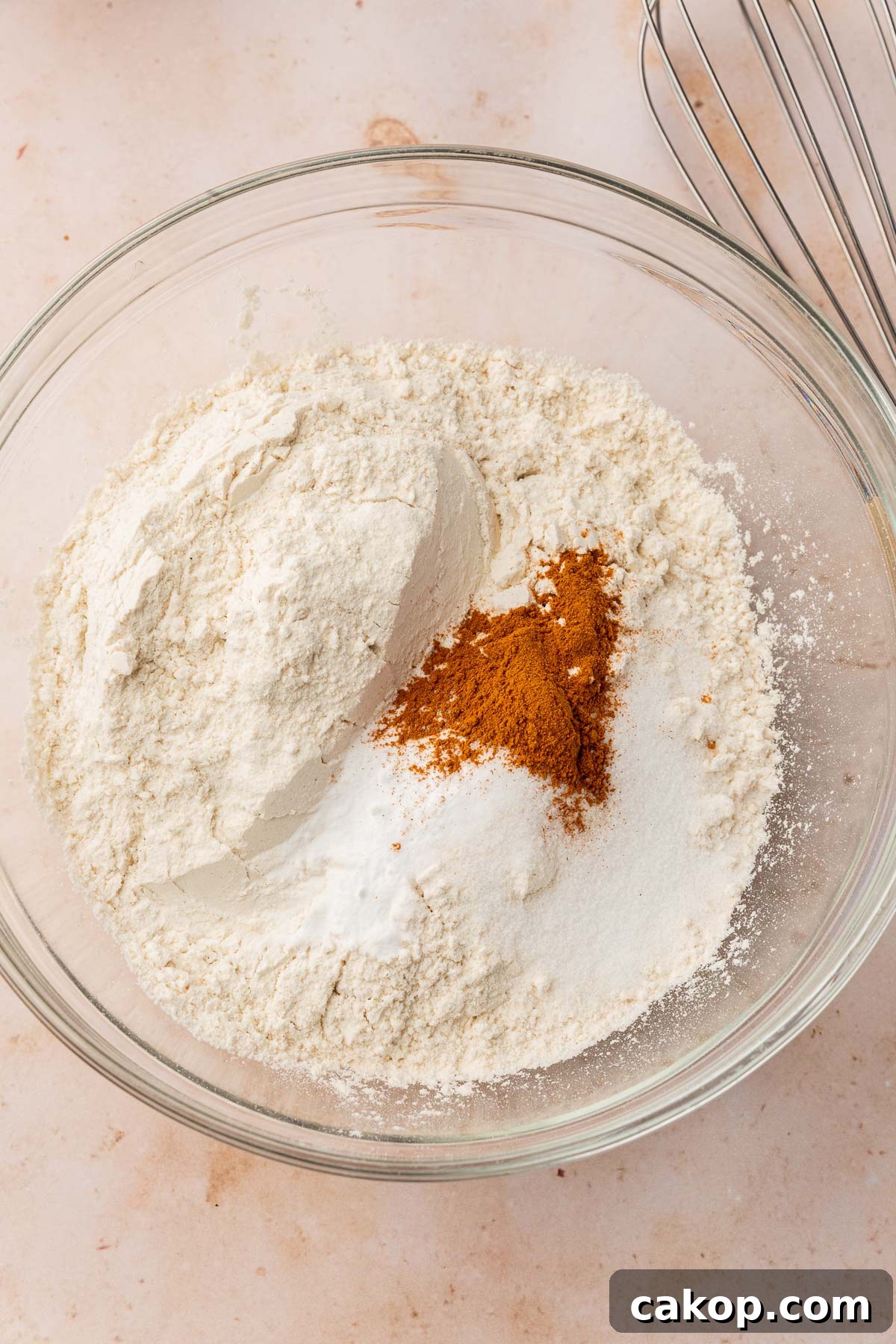 A glass mixing bowl with gluten-free flour, cinnamon, salt and baking soda in it before mixing together.
