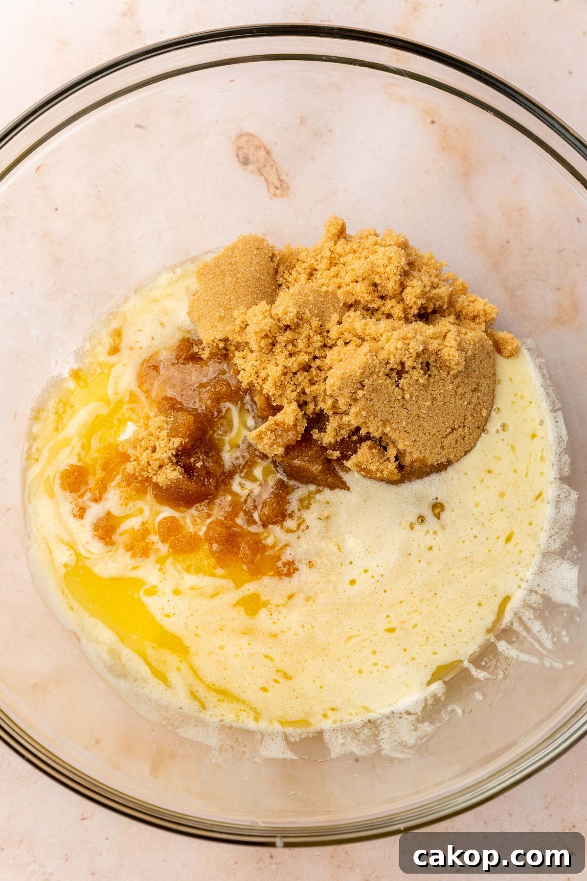 A glass mixing bowl with melted butter topped with brown sugar and granulated sugar.
