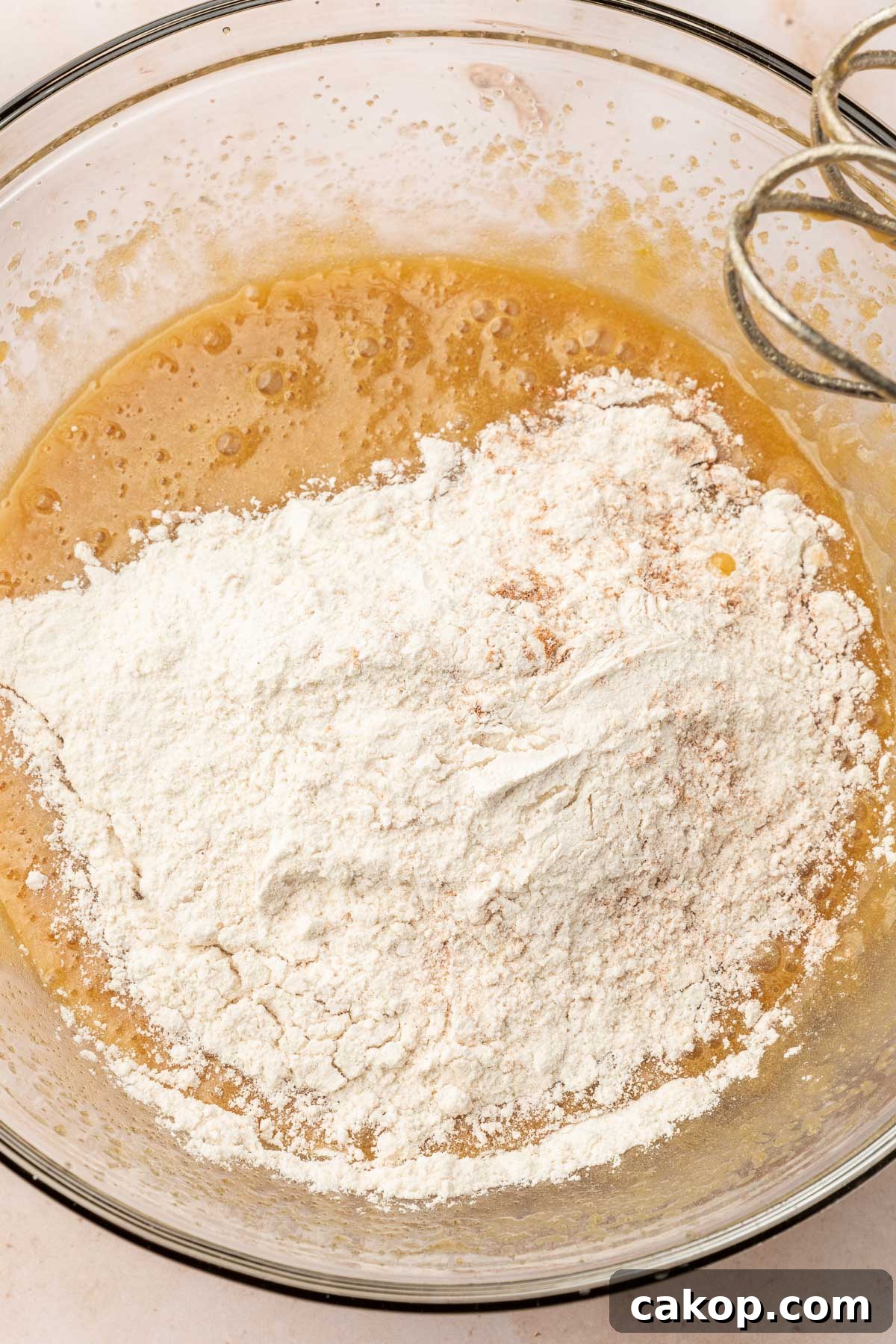 A glass mixing bowl with gluten-free cookie dough topped with gluten-free flour before mixing together.