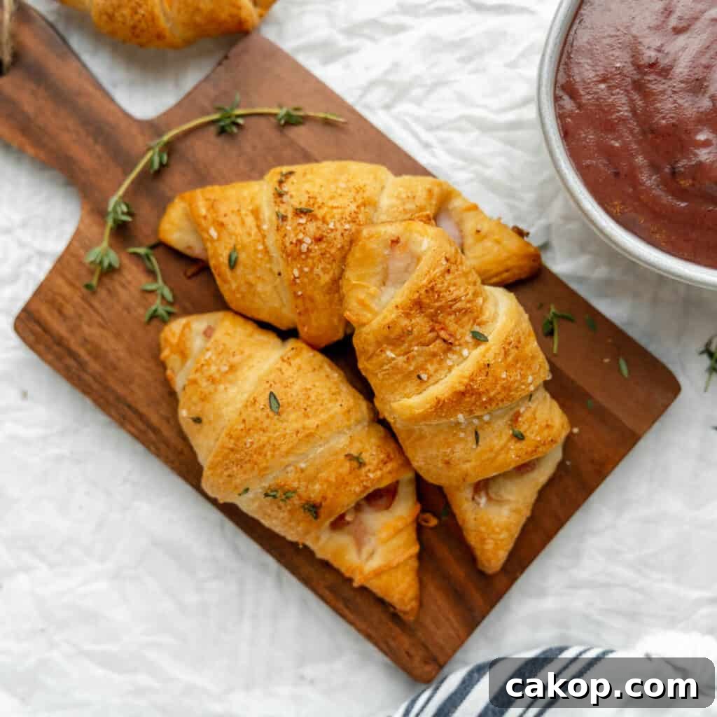 Three ham and cheese crescent rolls on a wooden cutting board.