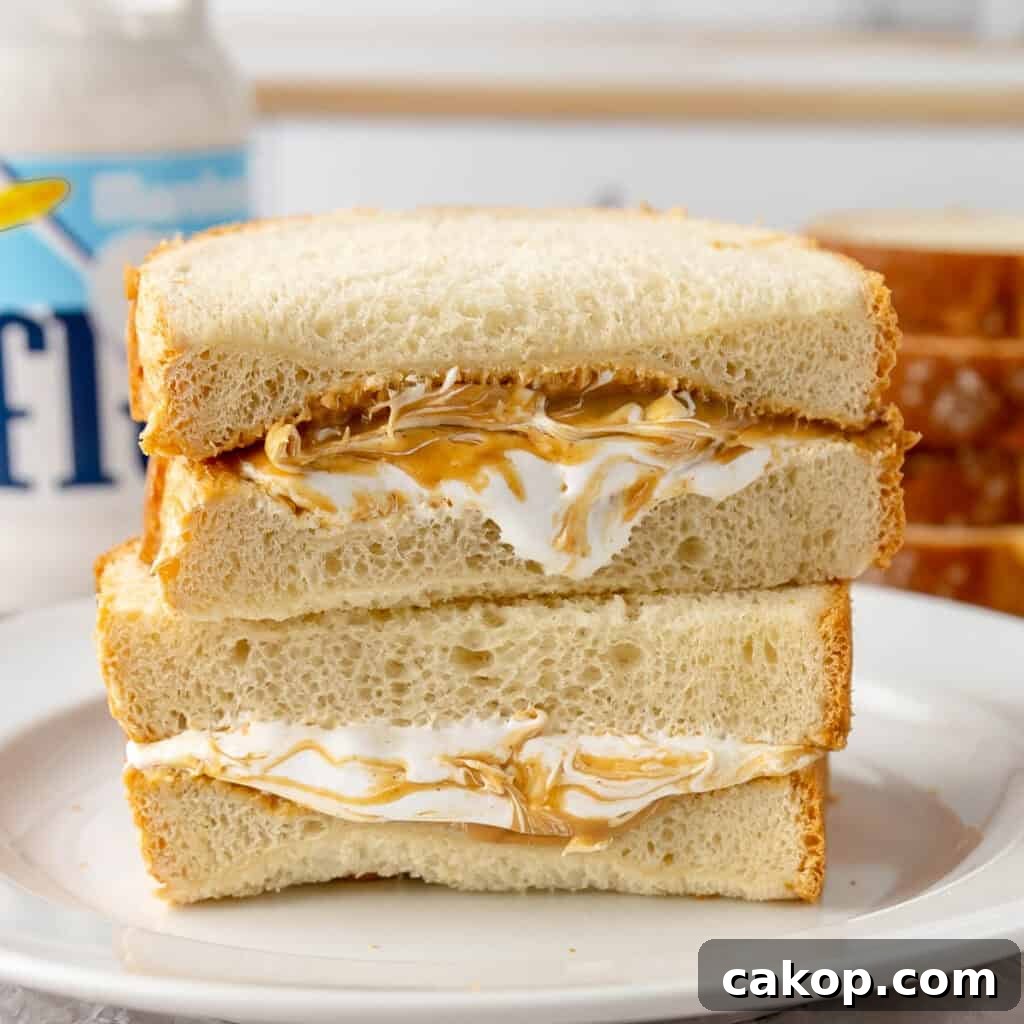 A close-up of a sandwich made with two slices of bread filled with peanut butter and marshmallow creme, sitting on a white plate.