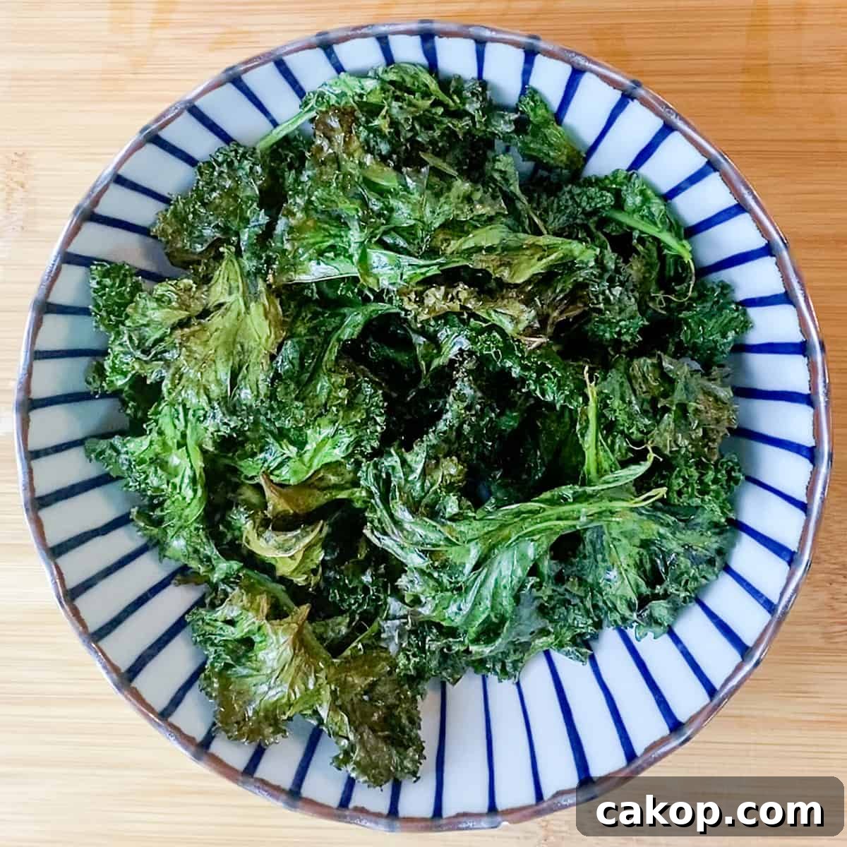 Photo of a blue and white stripy bowl filled with crispy kale, on a wooden surface.