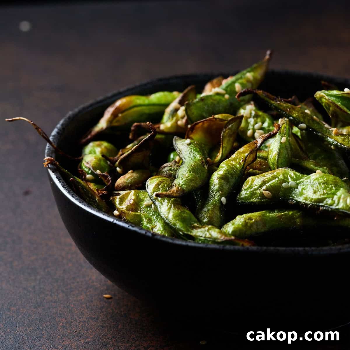 Crispy Air Fryer Frozen Edamame: Quick Snack or Side 10 Photo of a black bowl filled with air fryer frozen edamame beans set on a rusted black surface.