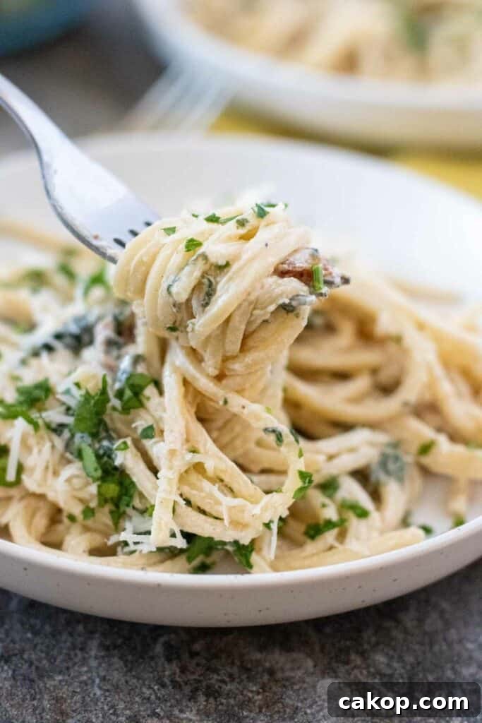 A fork is lifting a twirl of Creamy Tuscan Pasta garnished with chopped parsley and grated cheese from a white plate.