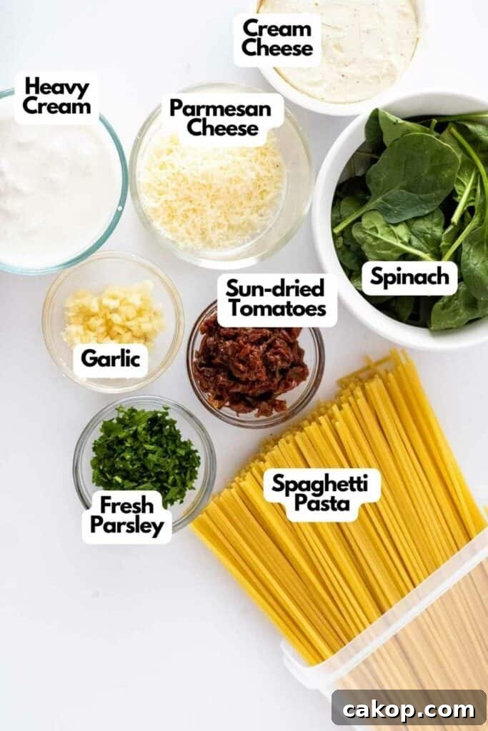 Ingredients for a Creamy Tuscan Pasta dish including heavy cream, cream cheese, Parmesan cheese, spinach, garlic, sun-dried tomatoes, fresh parsley, and spaghetti pasta displayed in bowls.