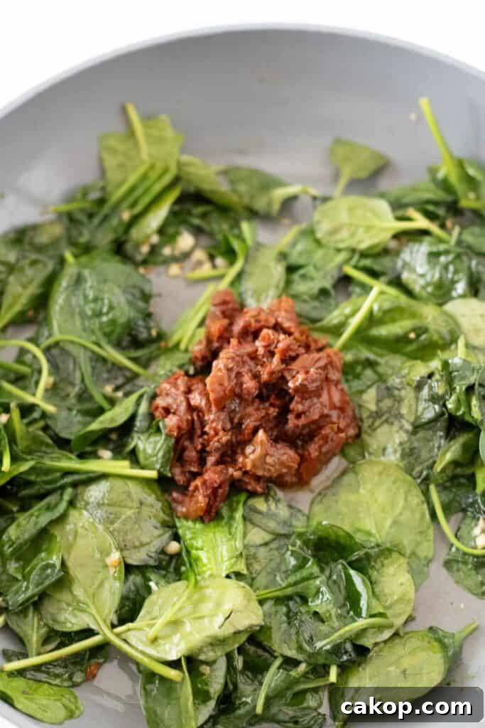A pan with sautéed spinach surrounding a mound of chopped sun-dried tomatoes at the center, evoking the vibrant flavors of Creamy Tuscan Pasta.