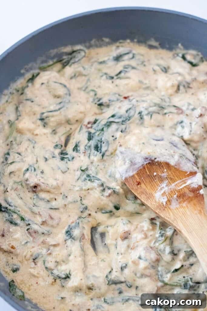 A creamy spinach and artichoke dip being stirred with a wooden spoon in a pan, looking just as indulgent as a Creamy Tuscan Pasta.