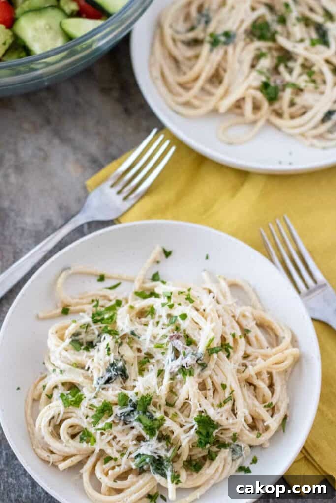 Two plates of creamy Tuscan pasta garnished with chopped herbs, with a side salad in the background. Two forks are placed on a yellow napkin next to one of the plates.
