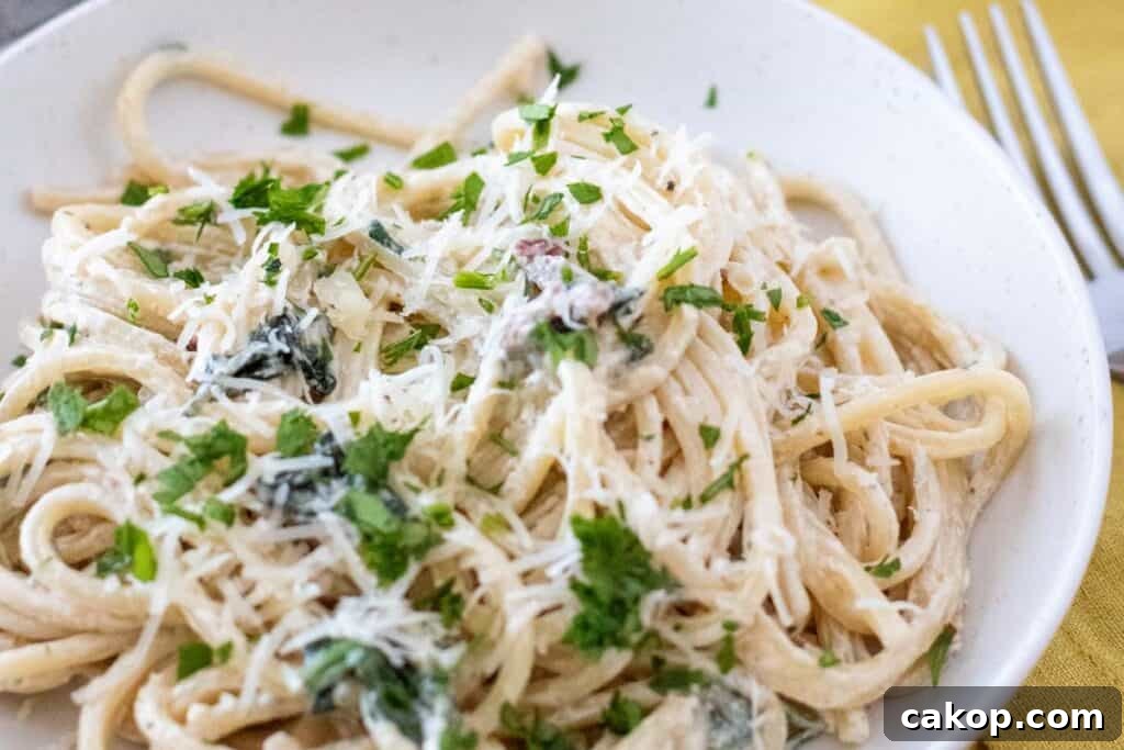 A plate of Creamy Tuscan Pasta garnished with chopped parsley and grated cheese sits on a table next to a fork.