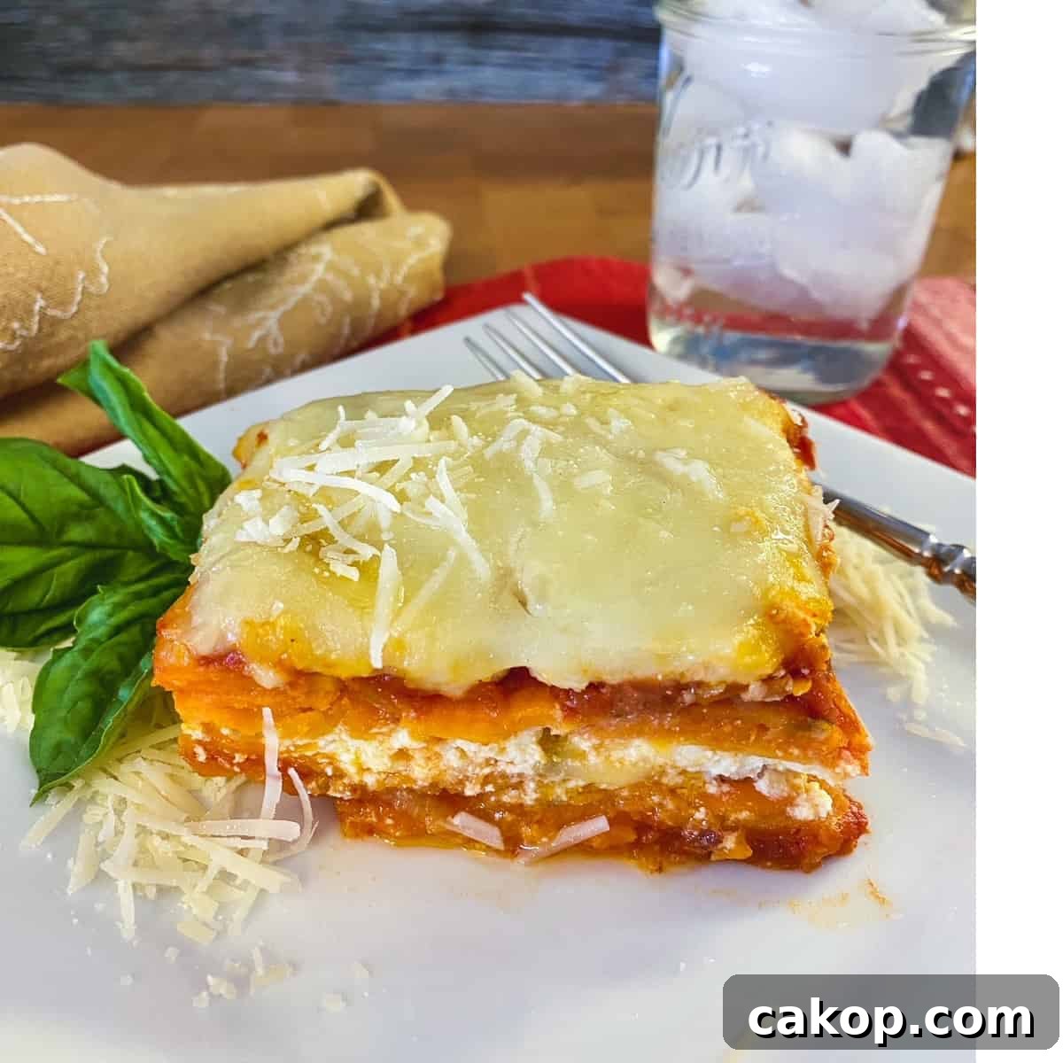 Sweet Potato Lasagna Recipe with Creamy Ricotta and Spinach 15 A slice of sweet potato lasagna on a plate with a glass of ice water on the side.