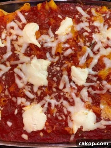 A large baking dish full of baked ziti pasta with small mounds of ricotta cheese on top.
