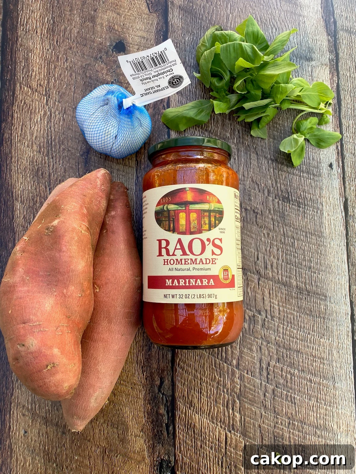 Sweet Potato Lasagna Recipe with Creamy Ricotta and Spinach 4 Ingredients arranged on a wooden plank, sweet potatoes, marinara sauce in a jar, fresh basil and a bulb of elephant garlic.