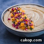Side angle shot of butternut squash roasted hummus with cubed butternut roasted squash, pomegranate seeds, pastel, pinuts, sumac and flaky sea salt on top.